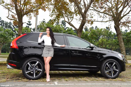 Asian model with long black hair in a skirt poses confidently beside a black Volvo car in a scenic outdoor setting, captured as an HD PC desktop wallpaper.