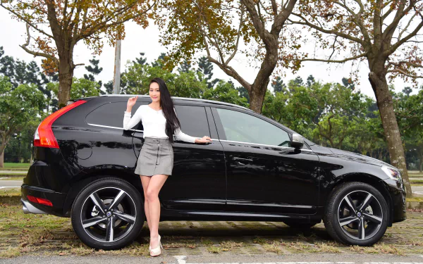 Asian model with long black hair in a skirt poses confidently beside a black Volvo car in a scenic outdoor setting, captured as an HD PC desktop wallpaper.