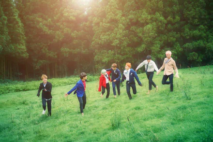 HD desktop wallpaper of BTS, a renowned K-pop group, featuring members holding hands and running through a lush green field with a forested background.