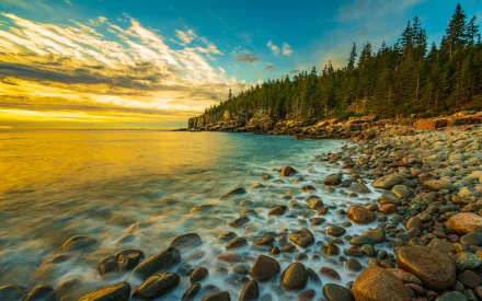 HD PC desktop wallpaper of Maine's rocky coastline at sunset, featuring ocean waves, a forested shoreline, and a vibrant sky over a natural beach setting.