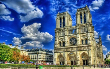 Vibrant HD image of Notre-Dame de Paris, showcasing its iconic facade against a dramatic blue sky with fluffy clouds, set in the heart of Paris.