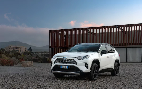 White Toyota RAV4 SUV parked on gravel in front of a modern building under a clear blue sky, captured in a 4K Ultra HD PC desktop wallpaper style.