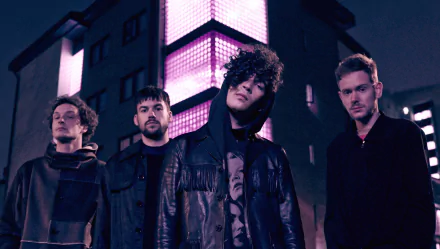 HD desktop wallpaper featuring The 1975 band members standing together at night with urban lighting in the background.