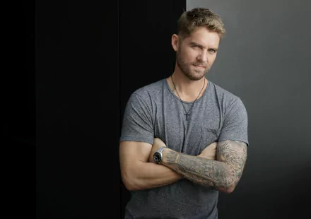 HD wallpaper featuring a confident man with crossed arms and tattoos, set against a dark background.