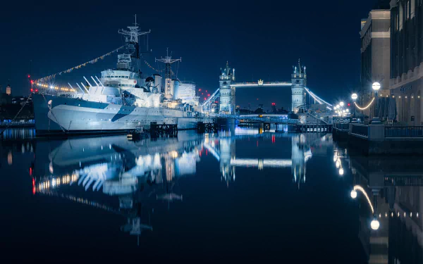 A night view of London featuring HMS Belfast (C35) and Tower Bridge, beautifully reflected in the water. The image serves as an HD desktop wallpaper and background.